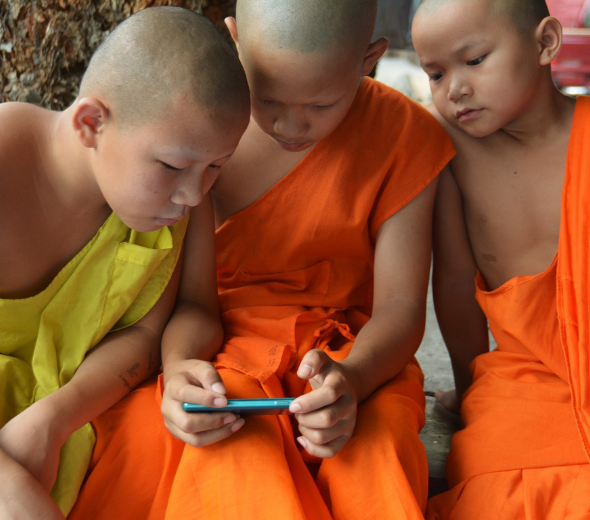 três crianças monges observando um smartphone